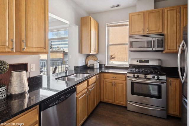 kitchen with kitchen peninsula, dark hardwood / wood-style flooring, stainless steel appliances, sink, and dark stone countertops