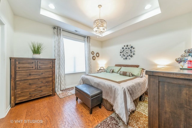 bedroom featuring a tray ceiling, a chandelier, and light wood-type flooring