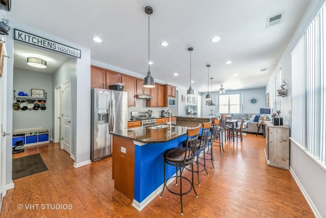 kitchen featuring appliances with stainless steel finishes, dark hardwood / wood-style floors, decorative light fixtures, sink, and a kitchen island with sink