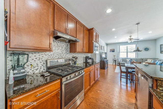 kitchen featuring appliances with stainless steel finishes, pendant lighting, tasteful backsplash, dark stone countertops, and light hardwood / wood-style floors