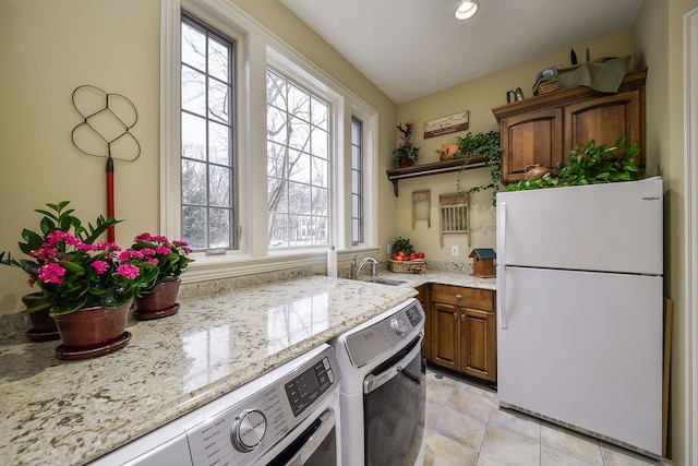 kitchen featuring light tile patterned flooring, sink, white refrigerator, light stone countertops, and washer and clothes dryer