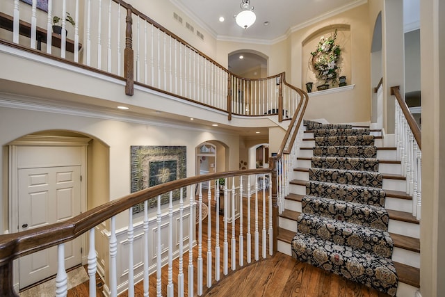 stairs featuring ornamental molding, a towering ceiling, and hardwood / wood-style floors