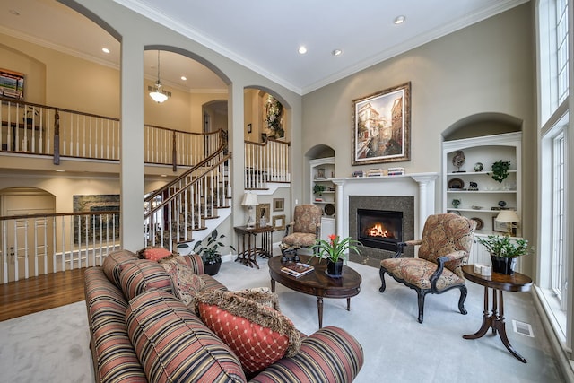 living room with a towering ceiling, crown molding, carpet flooring, and built in shelves