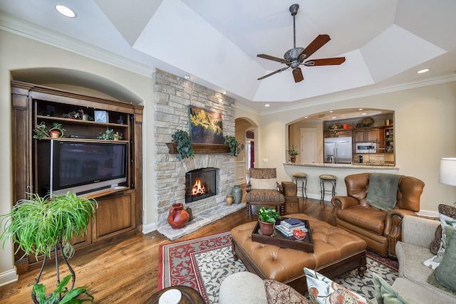 living room with lofted ceiling, crown molding, a fireplace, light hardwood / wood-style floors, and a raised ceiling