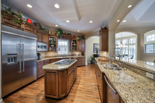 kitchen with sink, built in appliances, ornamental molding, a kitchen island, and light stone countertops