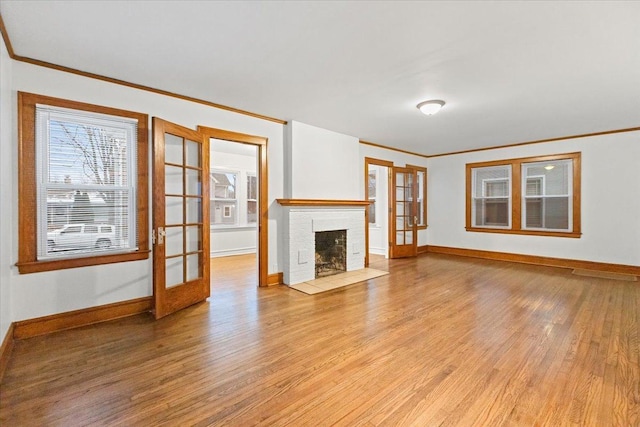 unfurnished living room with french doors, a brick fireplace, crown molding, and light hardwood / wood-style flooring