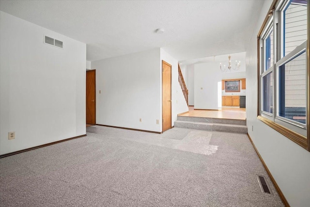 carpeted empty room with an inviting chandelier