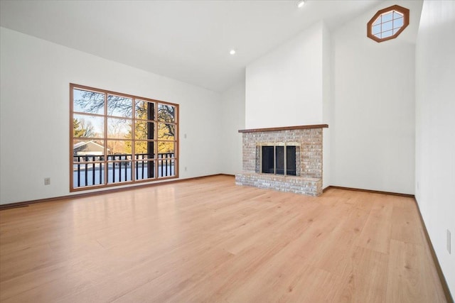 unfurnished living room with high vaulted ceiling, a brick fireplace, and light hardwood / wood-style floors