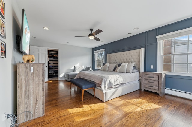 bedroom with a baseboard heating unit, hardwood / wood-style flooring, ceiling fan, and a spacious closet