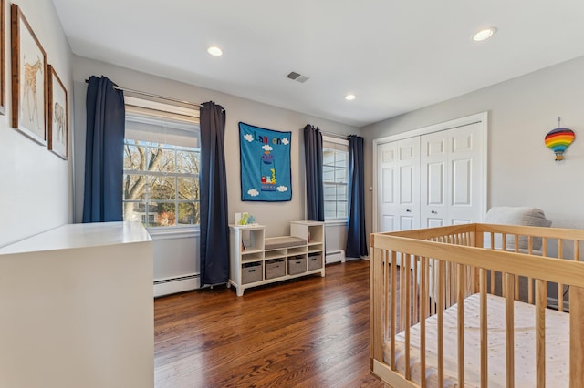 bedroom with multiple windows, dark hardwood / wood-style flooring, baseboard heating, and a closet