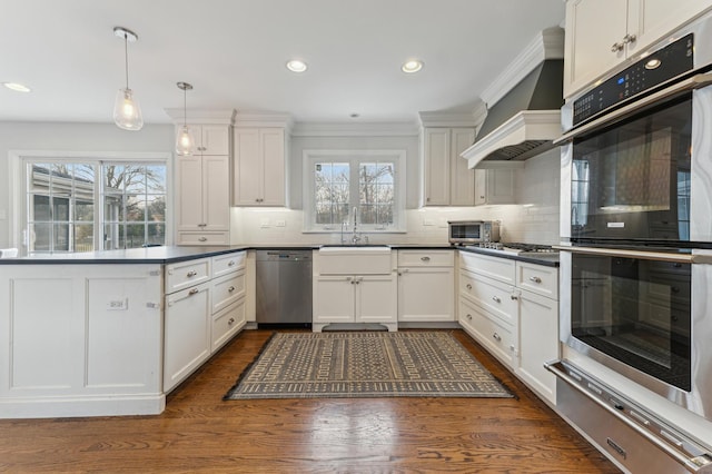 kitchen with sink, white cabinets, custom exhaust hood, hanging light fixtures, and stainless steel appliances