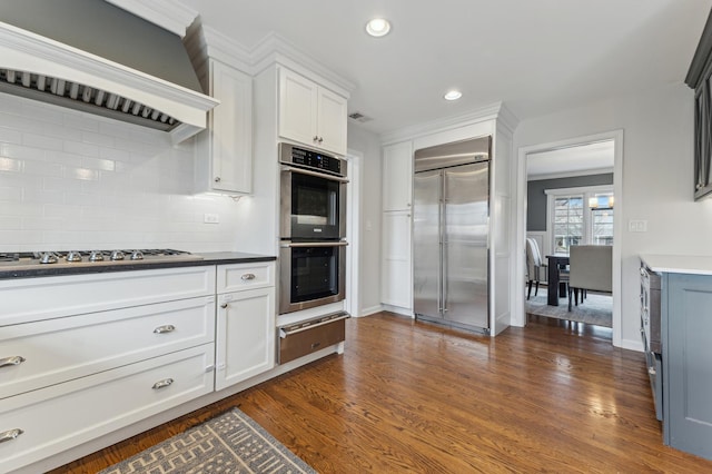 kitchen featuring dark wood-type flooring, premium range hood, white cabinetry, appliances with stainless steel finishes, and backsplash