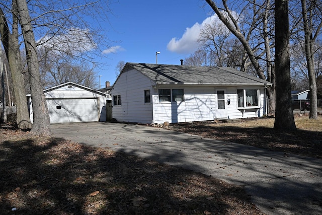 exterior space with a garage, a shingled roof, and an outbuilding