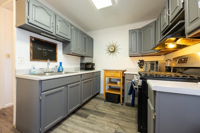 kitchen featuring black microwave, gray cabinetry, a sink, stainless steel range with gas cooktop, and light wood finished floors