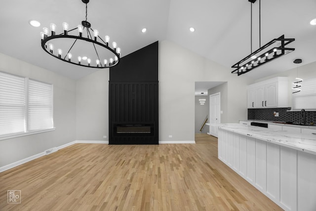 kitchen featuring light stone countertops, decorative backsplash, light hardwood / wood-style floors, white cabinetry, and hanging light fixtures