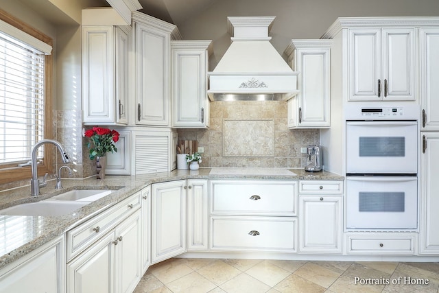 kitchen with white cabinetry, double oven, custom range hood, and sink