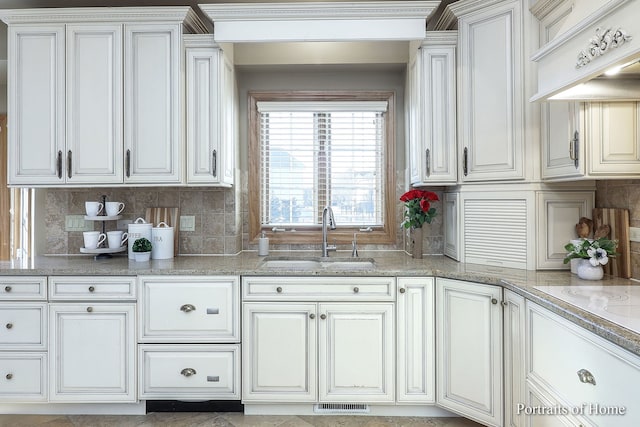 kitchen with tasteful backsplash, sink, custom range hood, white cabinets, and light stone counters