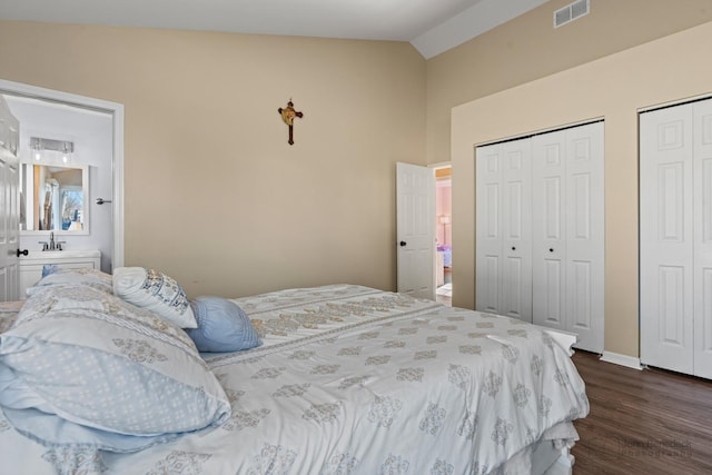 bedroom with vaulted ceiling, two closets, and dark hardwood / wood-style floors