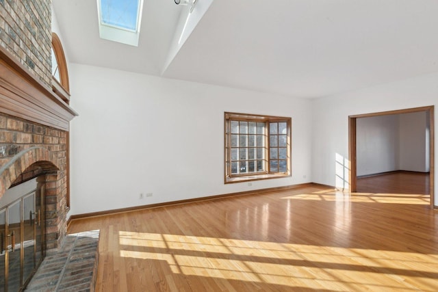 unfurnished living room with a brick fireplace, light hardwood / wood-style flooring, and vaulted ceiling with skylight