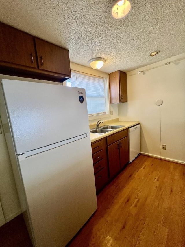 kitchen with a textured ceiling, sink, wood-type flooring, and white appliances