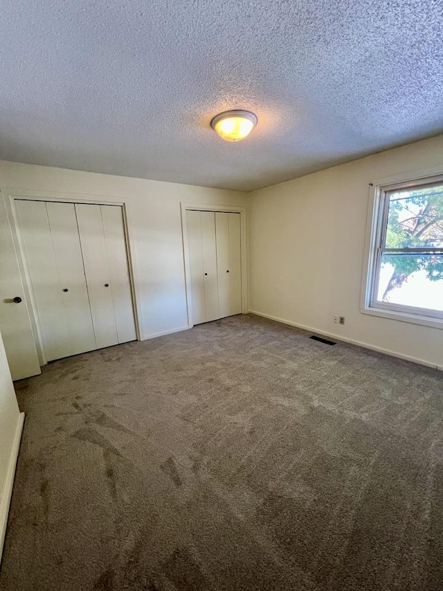 unfurnished bedroom with a textured ceiling, multiple closets, and carpet floors