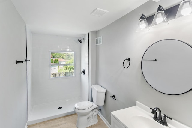 bathroom with a tile shower, vanity, hardwood / wood-style flooring, and toilet