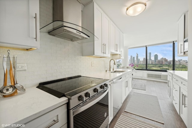 kitchen featuring white cabinets, wall chimney range hood, sink, high end stainless steel range, and light stone counters