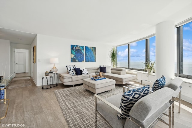 living room with expansive windows, a water view, and hardwood / wood-style flooring