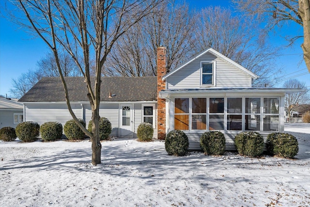 snow covered rear of property featuring a sunroom