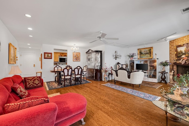 living room with ceiling fan with notable chandelier, rail lighting, and wood-type flooring