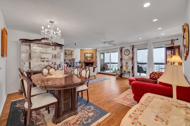 dining space with ceiling fan with notable chandelier, a fireplace, and light hardwood / wood-style floors