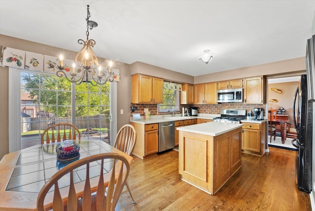 kitchen featuring a center island, hanging light fixtures, light hardwood / wood-style floors, decorative backsplash, and appliances with stainless steel finishes