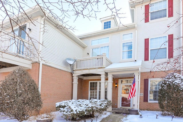 snow covered property entrance with a balcony