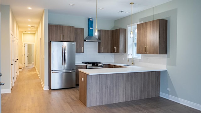 kitchen with stainless steel appliances, tasteful backsplash, light wood-type flooring, wall chimney range hood, and sink