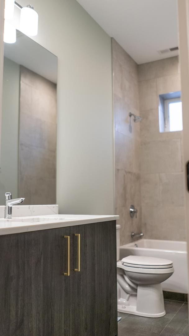 full bathroom with toilet, tile patterned flooring, tiled shower / bath combo, and vanity