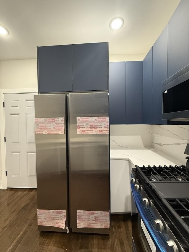 kitchen featuring blue cabinetry, stainless steel appliances, light stone counters, dark hardwood / wood-style floors, and decorative backsplash