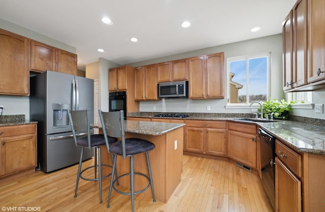 kitchen featuring a breakfast bar, a sink, light wood-type flooring, dark stone counters, and black appliances