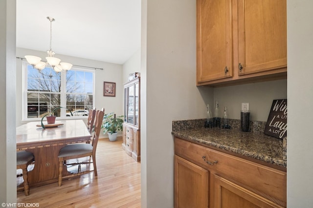 kitchen featuring dark stone counters, brown cabinets, hanging light fixtures, light wood-style floors, and a chandelier