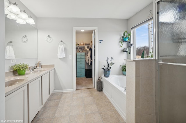 bathroom featuring a walk in closet, a garden tub, a sink, and double vanity