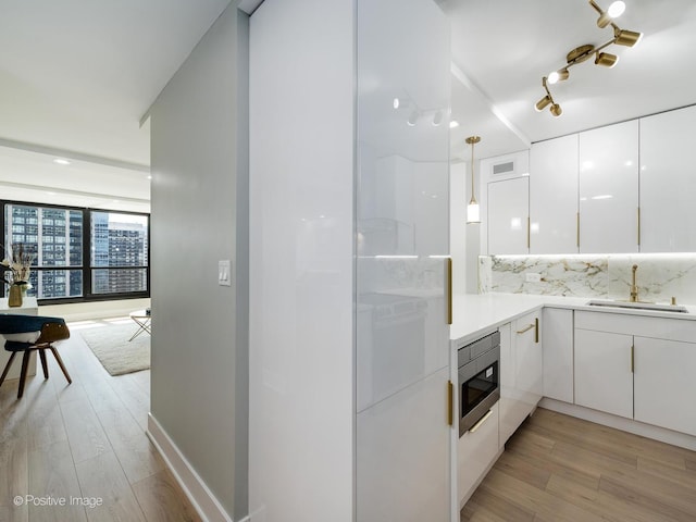 kitchen with sink, white cabinets, decorative light fixtures, and light wood-type flooring