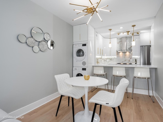 dining room with an inviting chandelier, stacked washing maching and dryer, and light hardwood / wood-style flooring