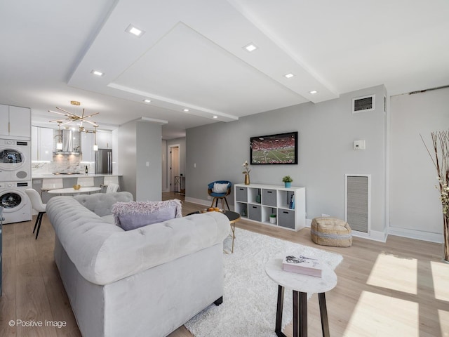 living room featuring stacked washer / drying machine, a chandelier, and light hardwood / wood-style flooring