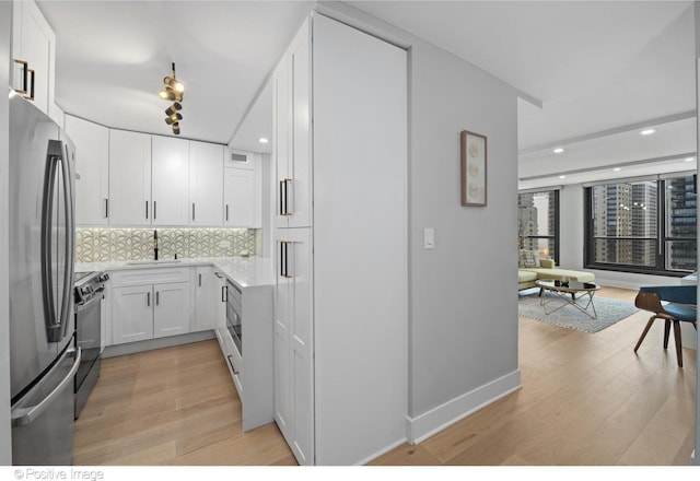 kitchen with white cabinets, sink, light hardwood / wood-style flooring, tasteful backsplash, and stainless steel appliances