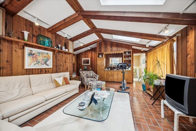 living room featuring rail lighting, vaulted ceiling with beams, and wooden walls