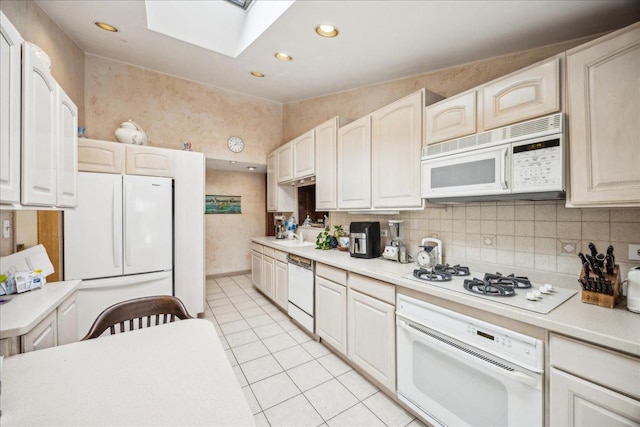 kitchen with a skylight, backsplash, white appliances, light tile patterned flooring, and white cabinets