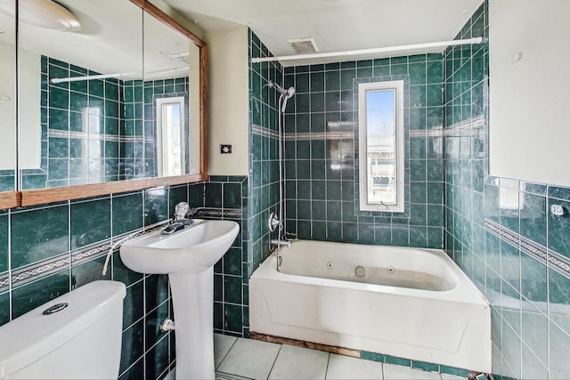 bathroom featuring tile patterned floors, tiled shower / bath, tile walls, and toilet