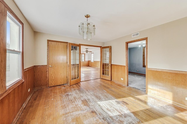 unfurnished dining area featuring wood walls, a chandelier, light hardwood / wood-style floors, and french doors