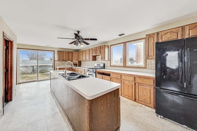 kitchen with black refrigerator, decorative backsplash, gas stove, a kitchen island with sink, and sink