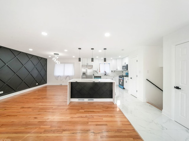 kitchen with sink, appliances with stainless steel finishes, white cabinetry, hanging light fixtures, and a center island