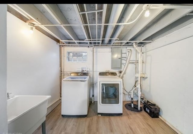 washroom with electric panel, sink, washer and clothes dryer, and light hardwood / wood-style floors